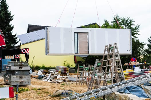 Construction of a prefabricated house with a house wall hanging from a crane.