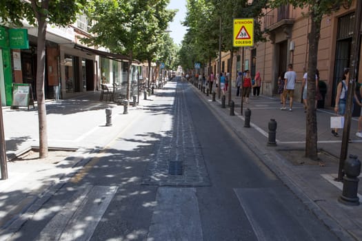 Granada, Spain - August 5, 2016: City center street a hot summer day with people walking on shadow sidewalk