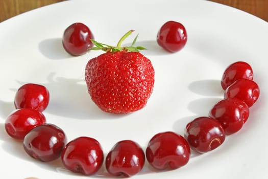smile made from berries of ripe red cherries and a strawberry on the white plate. Fresh strawberry and cherry