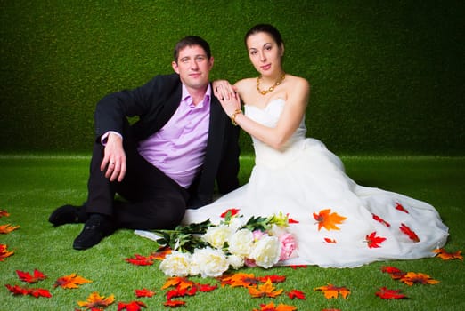Bride and groom sitting together on a green background and red maple leaf
