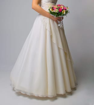 The beautiful bouquet of different colors in the hands of the bride in a white dress