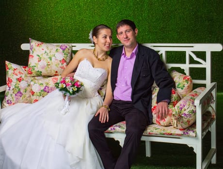 Bride and groom sitting together on a bench on green background
