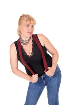 A woman in her forties standing in jeans and a black blouse with red.suspenders and a necklace, isolated for white background..