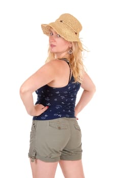 A middle age blond woman standing in shorts from the back in a straw hat, .looking over her shoulder isolated for white background..