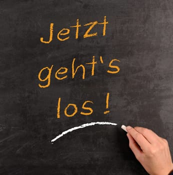Hand writing with chalk on a blackboard the German words "Start now!"""