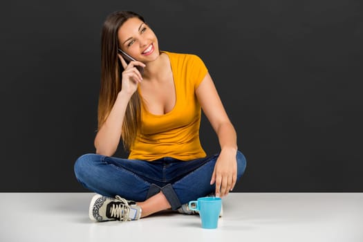 Beautiful young woman sitting in the floor in front of a dark wall
