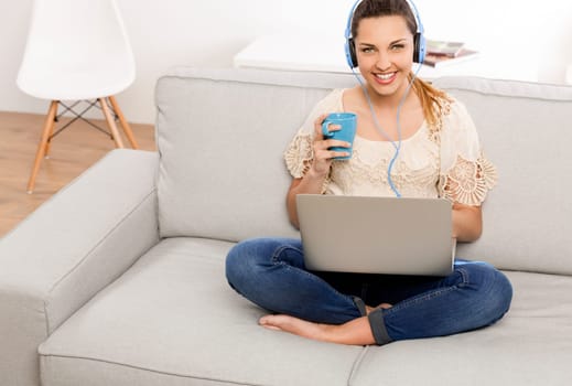Beautiful woman at home working on her laptop and listening music
