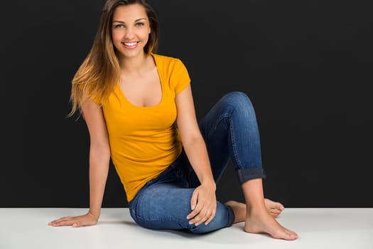 Beautiful young woman sitting in the floor in front of a dark wall