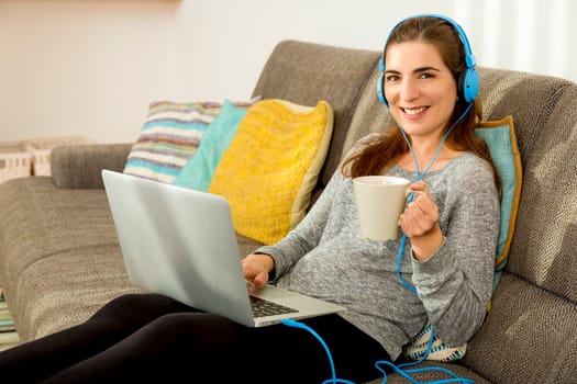 Beautiful woman working at home with a laptop while listen music and drinking coffee