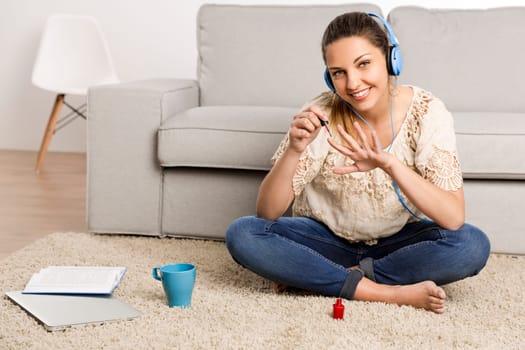 Beautiful woman at home making a pause to painting her nails while listening music