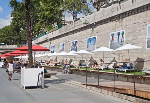 people lying in the sun on the banks of the seine in paris