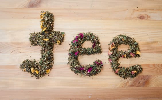 Tea lettering made of loose tea on rustic background made of wood