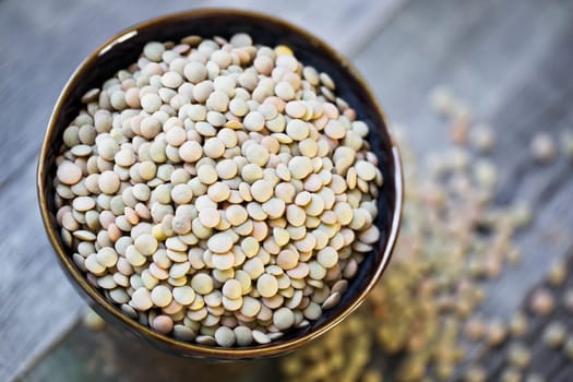 Fresh dried green lentils in ceramic bowl set on wooden table