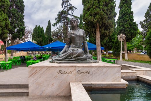 Shaki, Azerbaijan - May 13, 2024: A statue of the 12th-century Azerbaijani poet Mahsati Ganjavi stands elegantly amidst a verdant setting, complemented by outdoor seating and lush greenery