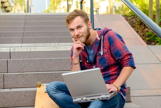 young man in checkered shirt sitting on stairs and using laptop