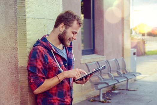 young man in checkered shirt standing on house wall and using tablet PC