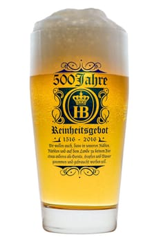 Munich, Germany - June 11, 2016: Glass of cold Bavarian beer with frothy foam head backlit isolated on white with text 500 years of Reinheitsgebot - German Beer Purity Law