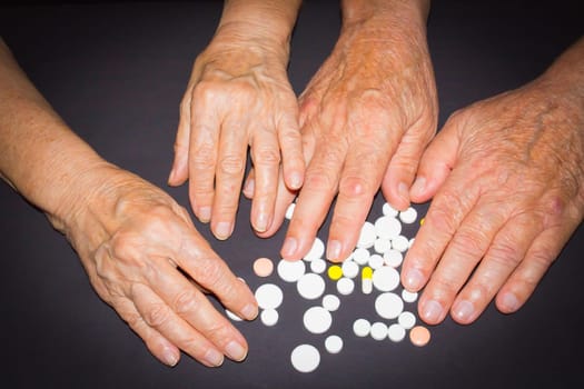 The old female and male hands with pills on black background