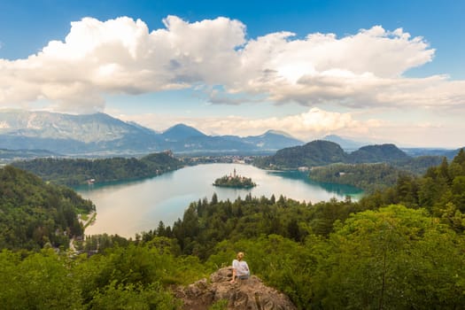 Relaxed female traveler enjoying beautiful panoramic view of Julian Alps, Lake Bled with St. Marys Church of the Assumption on the small island, Bled, Slovenia, Europe.