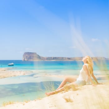 Relaxed woman enjoying sun, freedom and life an a beautiful sandy beach of Balos in Greece. Young lady feeling free, relaxed and happy. Vacations, freedom, happiness, enjoyment and well being.