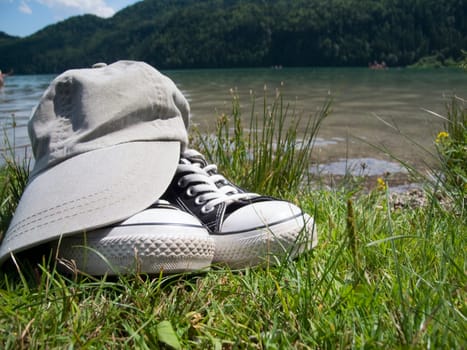 Wide-angle close-up on green grass of fabric sports shoes with a schirmütze placed on it in summer at the Weissensee in the East-Allgäu