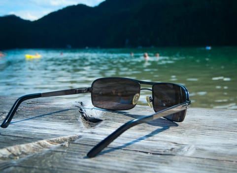Close-up of sunglasses lying on a wooden jetty and fuzzy lake in the background