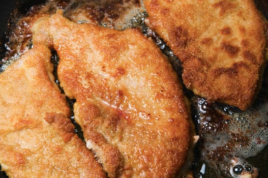 Close-up of a frying pan with two golden-yellow slices of schnitzel meat frying in it