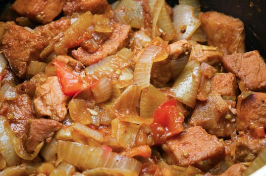 Close-up steaming meat cubes with pieces of pebbles and tomato pieces of a goulash dish in black stew