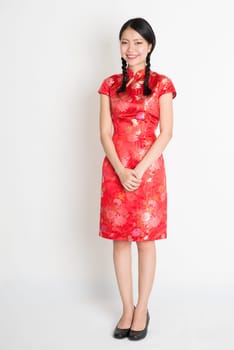 Portrait of full length Asian Chinese female, in traditional red cheongsam standing on plain background.