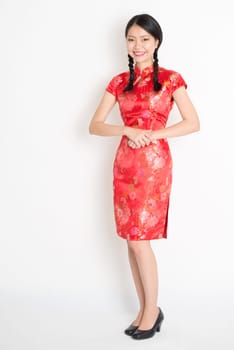 Portrait of full length Asian Chinese female, in traditional red qipao dress standing on plain background.