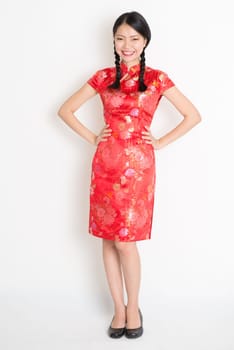 Portrait of full length Asian Chinese girl, in traditional red cheongsam standing on plain background.
