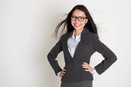 Beautiful young Asian business woman smiling at camera, standing on plain background.