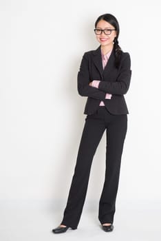 Full body Asian business woman smiling and standing on plain background.