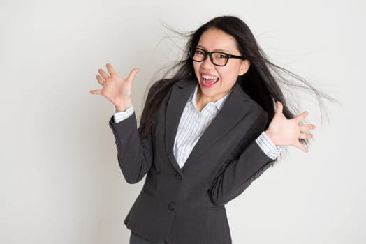 Surprised young Asian business woman smiling at camera, standing on plain background.