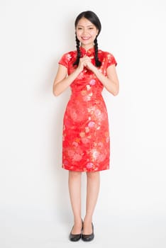 Happy Chinese New Year!! Portrait of Asian Chinese girl blessing, in traditional red qipao standing on plain background.