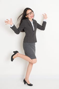 Excited full body Asian business woman cheering, standing on plain background.