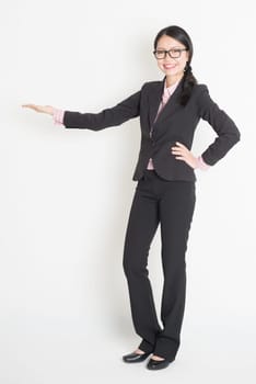 Full body Asian business woman showing copy space, hand holding something, standing on plain background.