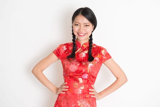 Portrait of Asian Chinese girl, in traditional red cheongsam standing on plain background.