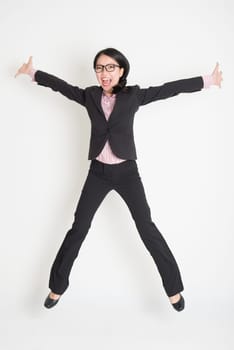 Full length of Asian successful business woman leaping high in the air, on plain background.