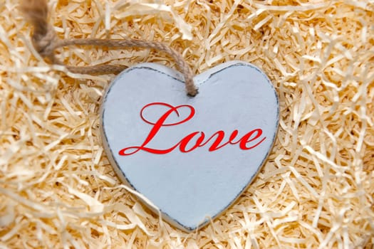 single grey wooden love heart in a love nest made of straw inscribed in red