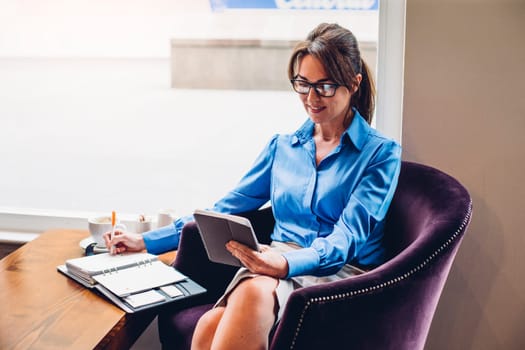 Mature business woman making notes and using a digital tablet in a cafe.