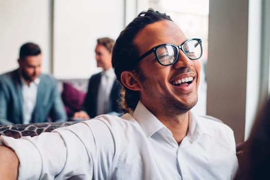 Close up shot of a business man laughing in a conversation with someone. Two men in suits can be seen talking in the background.