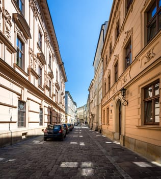Cars parked near houses in street in Krakow, Poland, Europe. Empty lane in morning. Blue sky and good weather for tourists.