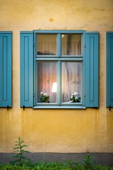 Details of old house window with flower and lamp inside. Yellow wall of building. Stockholm, Sweden, Scandinavia, Europe.