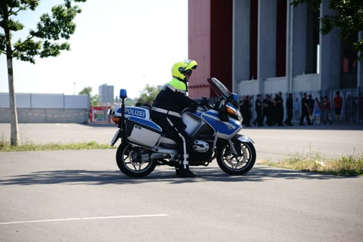 Mainz,Germany – August 06,2016: A policeman on a motorcycle watches fans in front of the entrance of the Opelarena at a football match of the 1st FSV Mainz 05 on August 6,2016 in Mainz.