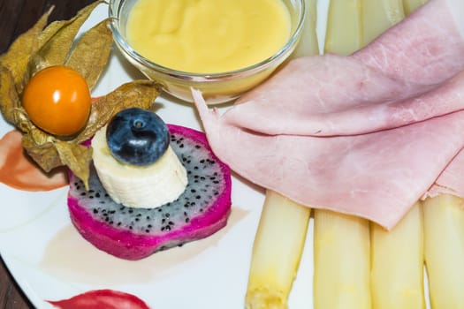 Simple asparagus dish with cooked ham and sauce garnned on a white plate. .