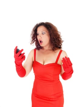A beautiful young woman looking very surprised at her cell phone, .standing in a red dress isolated for white background..