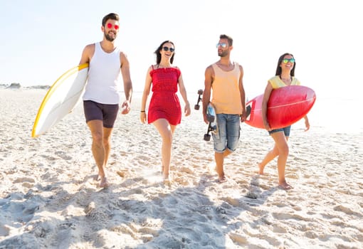 Group of friends walking together at the beach and holding surfboards