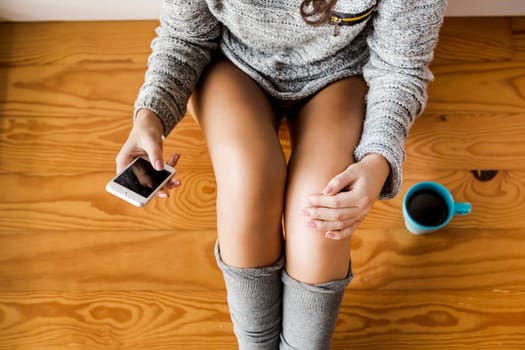 Woman sitting on the floor drinking a coffee and texting