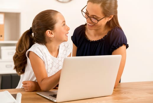Mother helping her little daughter how to use a computer